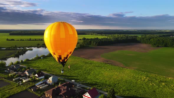 Yellow balloon with balloonist above field glows in dazzling rays of setting sun alt