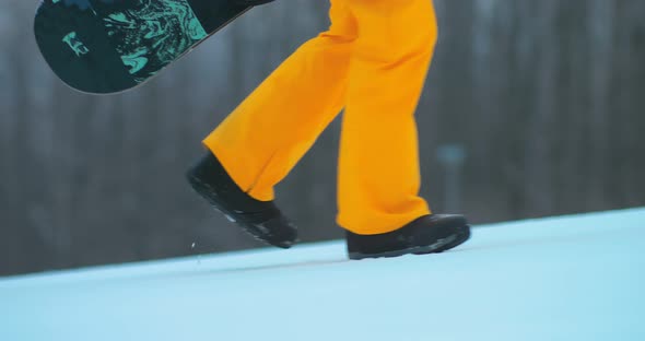 Snowboarder Rises Up the Track, Holds a Snowboard in His Hands. Snowboarder Legs Rise Uphill on a alt