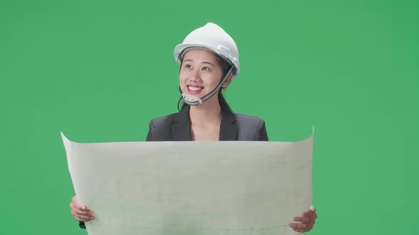 Smiling Asian Female Engineer Looking At Blueprint In The Green Screen Studio alt