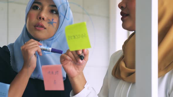 Two young Muslim businesswomen discussing a work in the office. alt