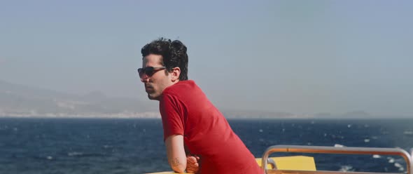 Man with sunglasses admiring the surrounding landscape leaning on the boat railing alt