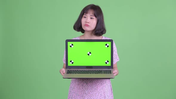 Happy Asian Pregnant Woman Thinking While Showing Laptop alt
