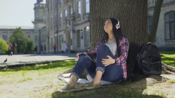 Asian Female in Headphones Enjoying Music, Sitting Under Tree, Favorite Band alt