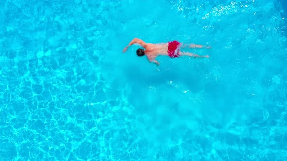View From the Top As a Man in Red Shorts Swims in the Pool alt