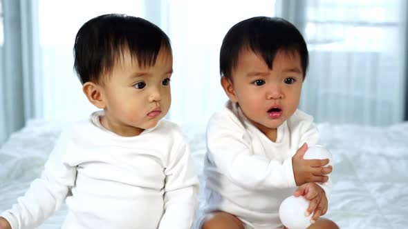slow-motion of cheerful twin babies playing color ball on a bed