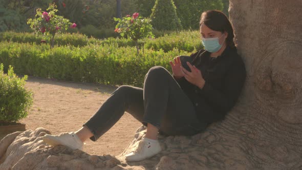 Brunette Girl in the Mask is Sitting in the Park