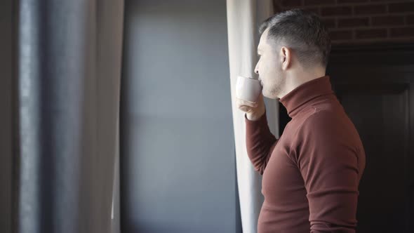 Side View of Confident Successful Man Drinking Coffee and Looking Out the Window alt