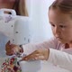 A Little Girl Is Sewing Fabric and Talking. Mom Is at the Background. Close-up