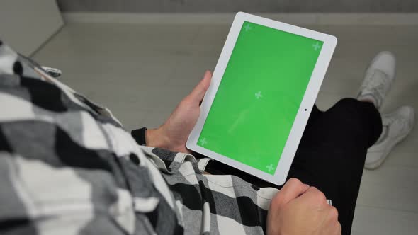 Man Sitting on Chair Looking at Digital Tablet with Green Screen Chroma Key alt