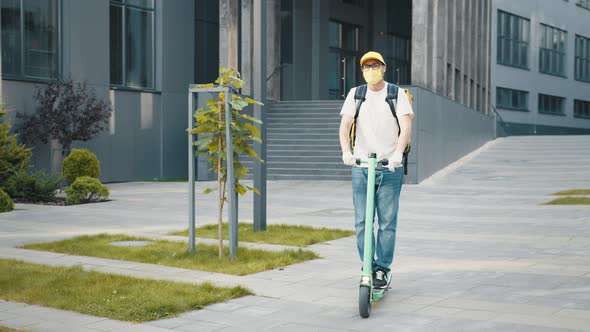 Delivery Man with Yellow Backpack and Protective Mask Riding Electric Scooter alt