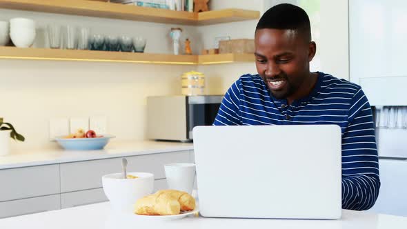 Man using laptop while having coffee in kitchen alt