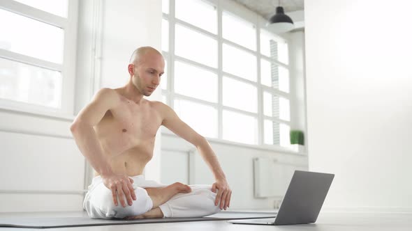 Bald Caucasian Shirtless Yogi Man Showing Exercises at Laptop Camera