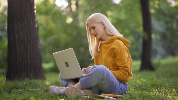 A Young Blonde Woman Communicates on Social Networks with Her Friends Via a Laptop