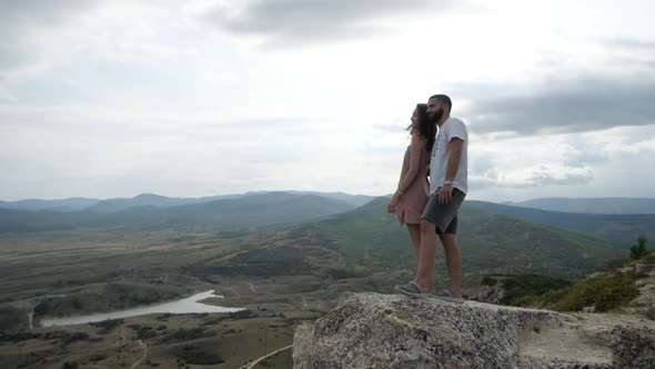 Girl and Guy Cuddling Stand on the Edge of the Cliff and Look Into the Distance