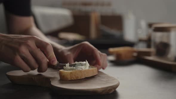 Slow Motion Man Spread Cream Cheese Over Ciabatta Slice on Olive Board alt