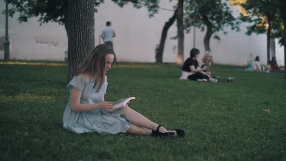 A girl reads a book on the grass in the park
