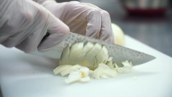 Chef finely dices yellow onion with steel knife, close up slow motion 4K alt