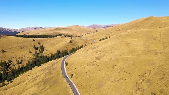 Aerial view of car driving down country road through rural rolling hills and mountain alt