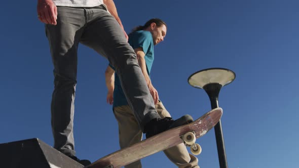 Low section of two male friends skateboarding on sunny day alt