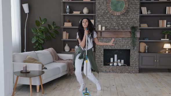 Happy Young Funny Woman Cleans in Modern Living Room Singing Song Using Mop As Microphone Active alt