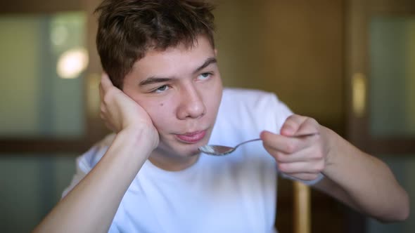 Teenager lazily puts rice porridge in his mouth and chews it alt