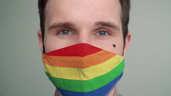 Close-up portrait of a young man with a black heart on his cheek wearing a rainbow face mask.