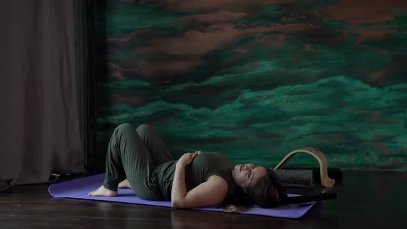 a Woman in a Green Jumpsuit is Lying on a Sports Mat alt