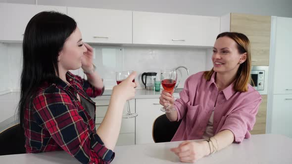 Happy Young Girls Drink Wine and Talk Sitting at Home in the Kitchen