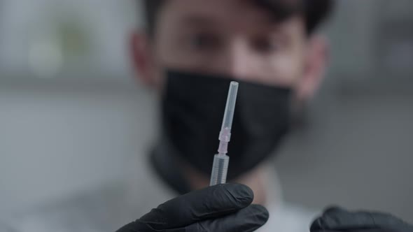 Closeup Syringe with Botox Filler Opening with Blurred Man in Coronavirus Face Mask at Background alt