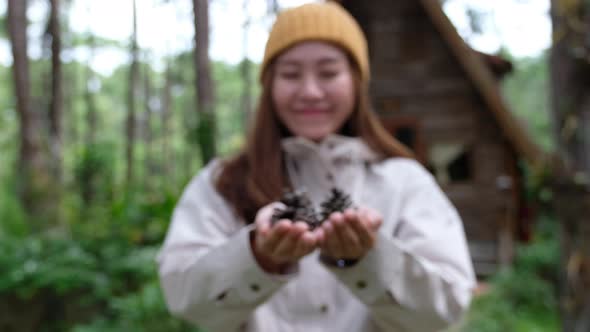 A young female traveler holding and showing pine cone in hands while traveling the forest