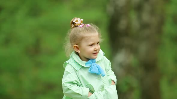 A little beautiful girl is talking and eating candy in a green forest.  It's spring.
