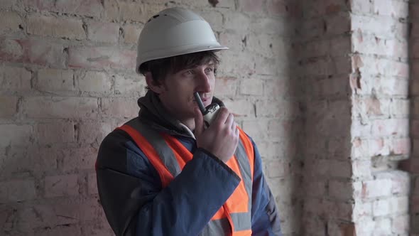 An angry builder speaks on a radio walkie-talkie to employees. alt