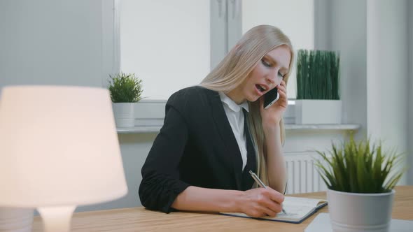 Business Woman Talking on Smartphone in Office. Elegant Young Blond Female in Office Suit Sitting at alt