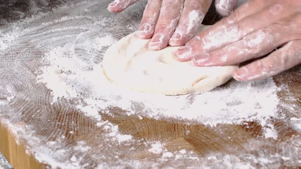 Human hands roll out fresh dough for make bread or pizza on kitchen board for baking. alt