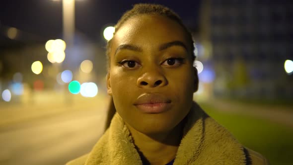 A Young Black Woman Looks Seriously at the Camera in a Street in an Urban Area at Night  Closeup alt