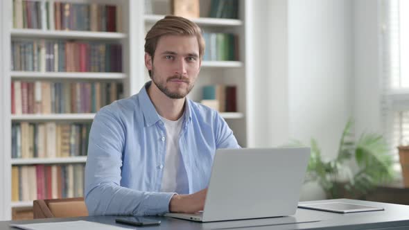 Man Smiling at Camera While Using Laptop in Office alt