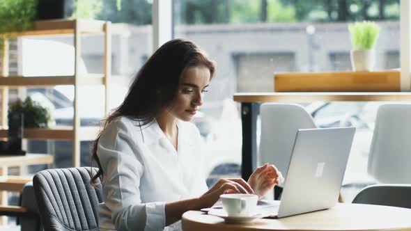 Confused and Baffled Woman Typing on Laptop in Cafe alt