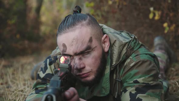 Portrait of Soldier Lies on a Forest Path and Aims with Rifle at Camera alt