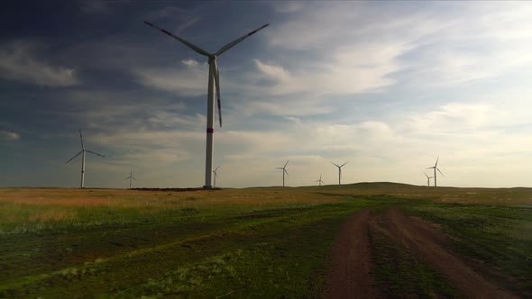 Motion the Blades of a Large Wind Turbine in a Field Against a Background of Cloudy Blue Sky Near