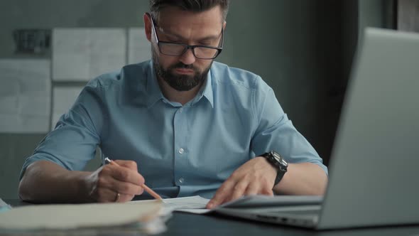 Bearded Man in Glasses Works Painstakingly in a Bright Office