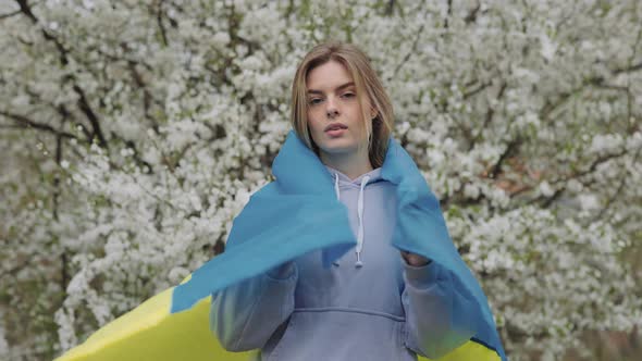 Patriotic Lady Wrapping in Ukrainian Flag in Blooming Garden alt