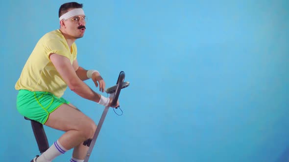 Funny Tired Man of the 80's with a Mustache and Glasses on the Exercise Bike on a Blue Background alt