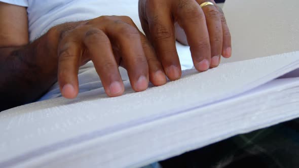 Close-up of blind senior man reading braille book in a comfortable home 4k alt