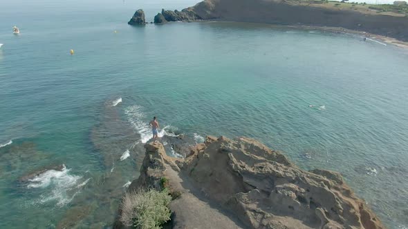 Aerial Shooting of a Young Attractive Man Standing on a Cliff  alt