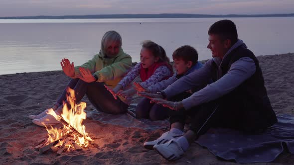Happy Family with Children Warm Hands By Fire on Beach
