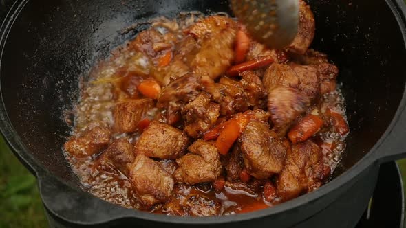 Cooking Process, Frying Pork Meat With Carrots and Onion in Large Cauldron on Open Fire.