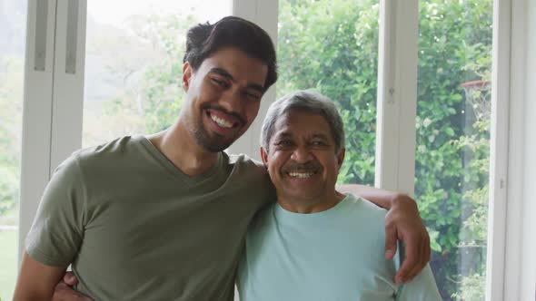 Portrait of cheerful biracial young man with hand on shoulder of father at home alt