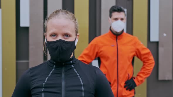Female and male athlete wearing protective face masks in front of wall