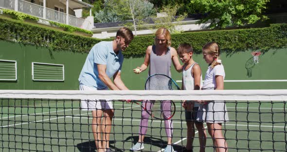 Caucasian father and mother teaching their kids to play tennis at tennis court on a bright sunny day alt