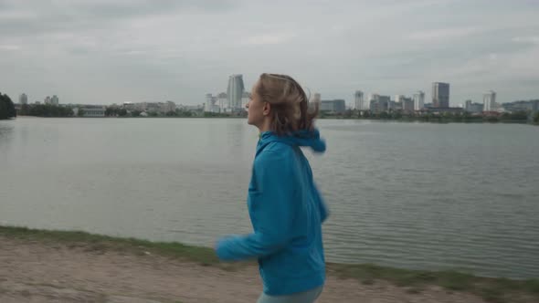 Young Sportswoman in Sportswear Trains in a Park Near the River alt